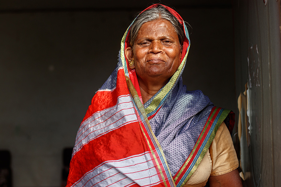Woman in a colorful head covering, who underwent cataract surgery after years of working in extreme heat and sun, pictured against a dark background
