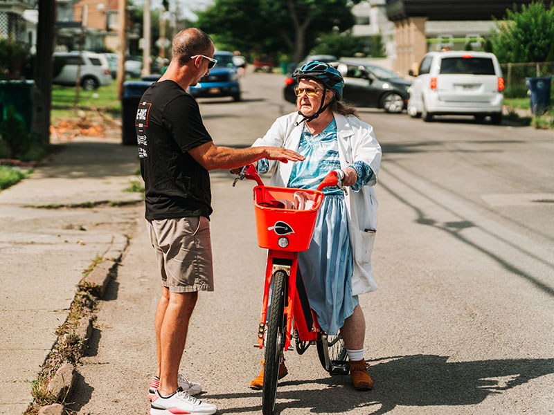 An elderly woman on an e-bike talks to a man standing beside her.