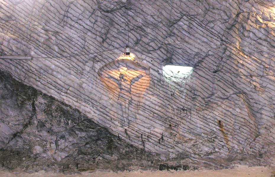 A wall of rock with distinct layers of deposits; Jesus on the cross is carved into the wall.