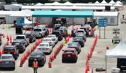 Photo shows lines of cars, flanked by construction cones, waiting in front of big white tents with Miami’s Hard Rock Stadium visible in the background.