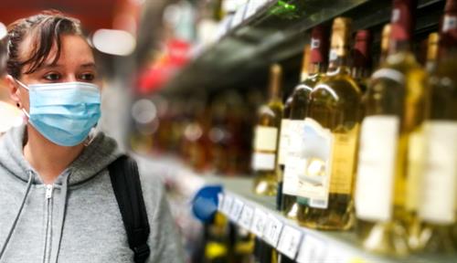 A woman wearing a surgical mask and gloves shops for alcohol in a store.